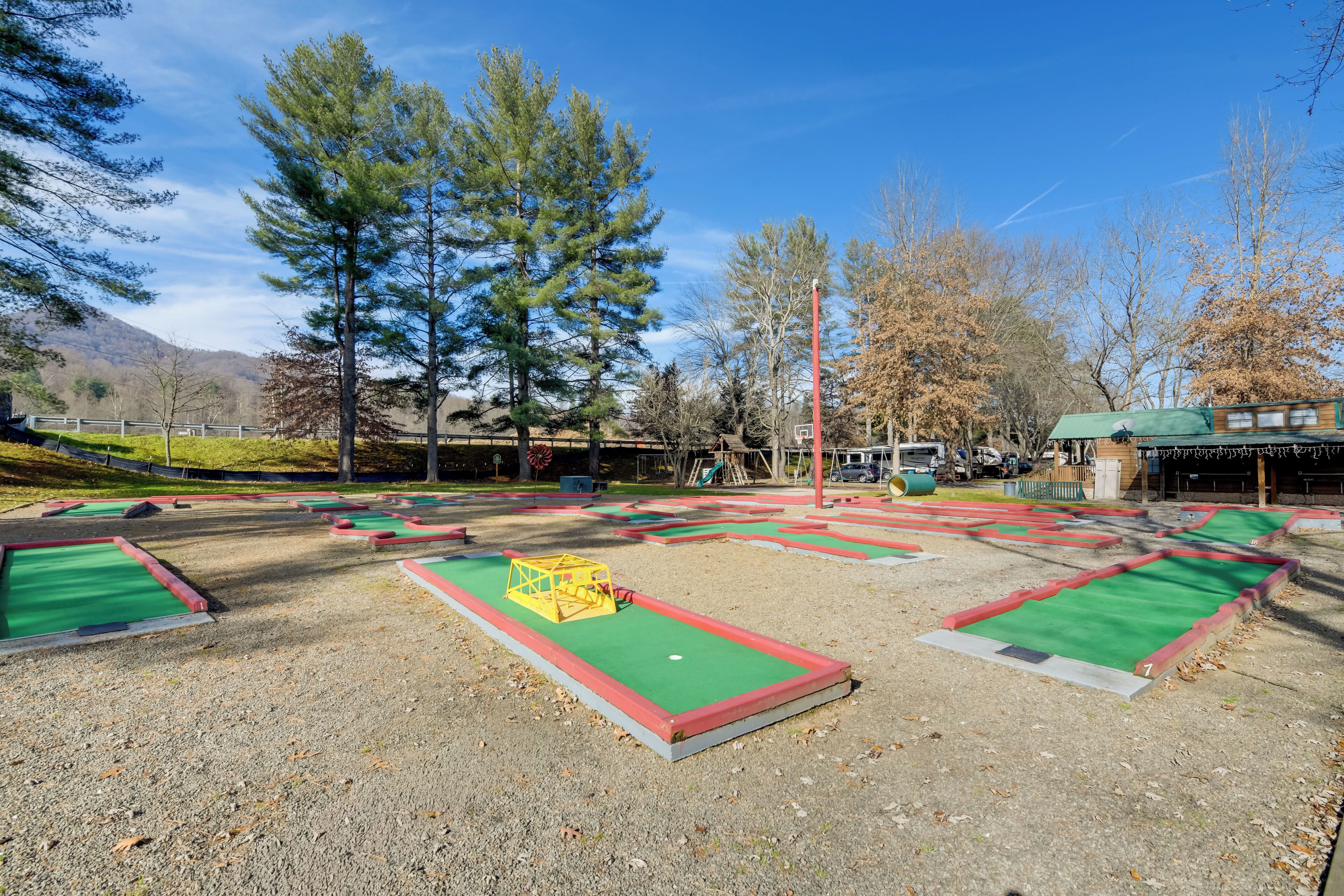 A miniature golf course with multiple holes, a green-roofed building, and a playground in the background.