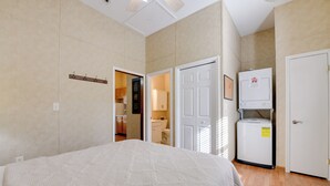 Un dormitorio con una cama, una puerta blanca y un pequeño electrodoméstico blanco, posiblemente un refrigerador o calentador, en la esquina.