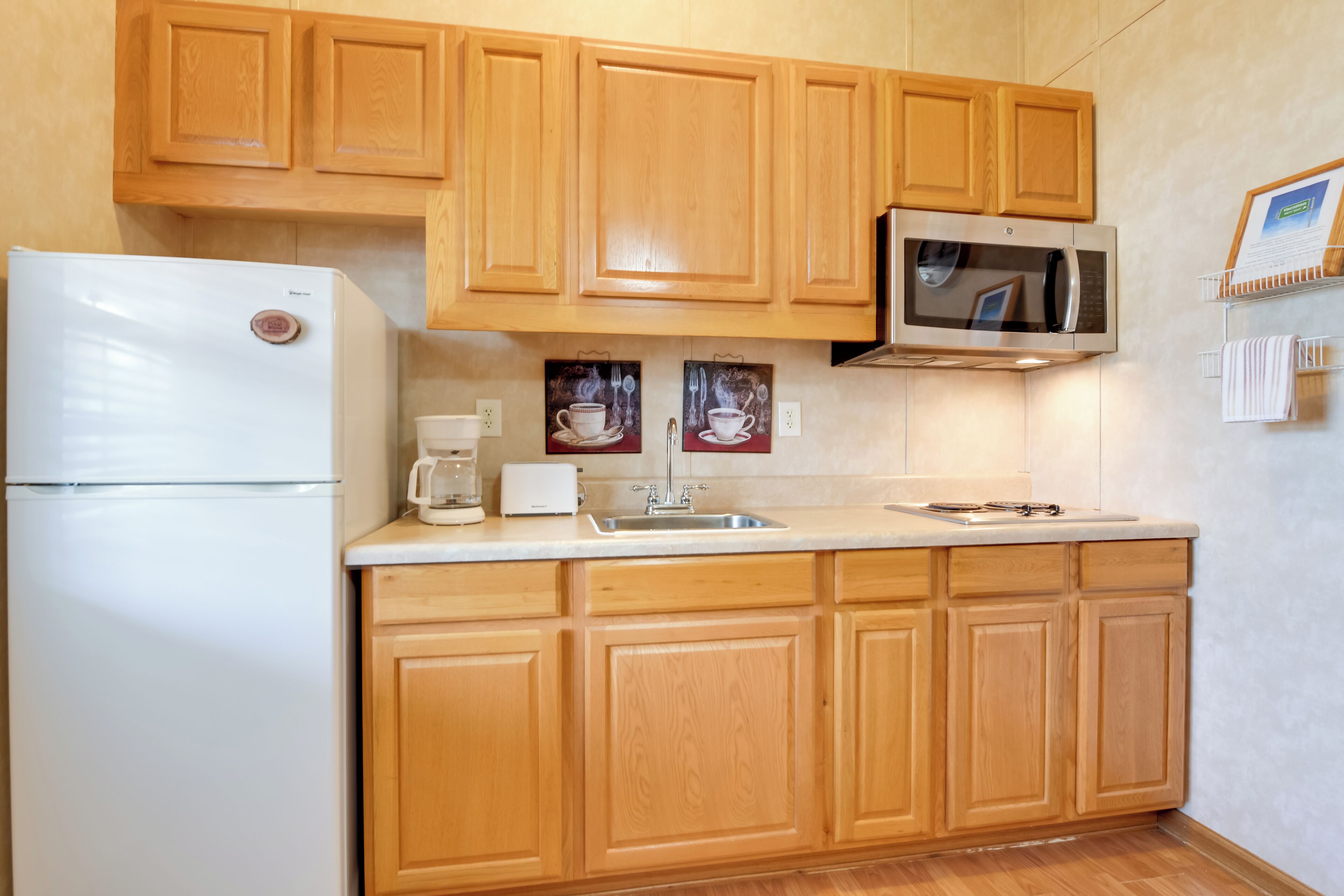 Una cocina con armarios de madera, un refrigerador blanco, un microondas y una cafetera.