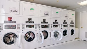 A row of white, stacked laundry machines with control panels and instructional signs. - Cozy Couples Getaway Near Cataloochee Ski Area! (Waynesville)