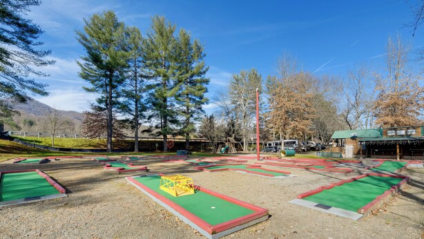 A miniature golf course with multiple holes, a green-roofed building, and a playground in the background. - Cozy Couples Getaway Near Cataloochee Ski Area! (Waynesville)