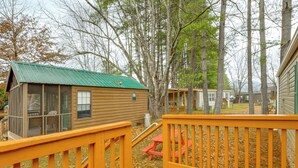 A wooden cabin with a green roof, a small porch with a red bench, and a view of surrounding trees and other cabins. - Near Trails & Slopes! Relaxed Waynesville Retreat (Waynesville)