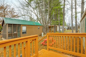 A wooden cabin with a green roof, a small porch with a red bench, and a view of surrounding trees and other cabins. - Near Trails & Slopes! Relaxed Waynesville Retreat (Waynesville)