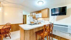 A compact kitchen with wooden cabinets, a white countertop, a microwave, a sink, and a flat-screen TV mounted on the wall. - Near Trails & Slopes! Relaxed Waynesville Retreat (Waynesville)