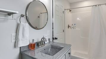 A bathroom with a granite sink, a mirror, a towel rack, and a shower area.