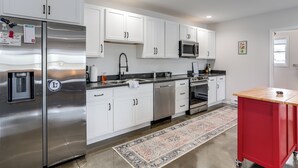 A modern kitchen with white cabinets, stainless steel appliances, a red utility cart, and a patterned rug. - Patio & Parking! Modern Bunkhouse Near Lake Erie (Oak Harbor)