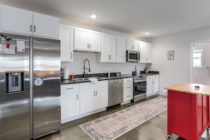 A modern kitchen with white cabinets, stainless steel appliances, a red utility cart, and a patterned rug. - Patio & Parking! Modern Bunkhouse Near Lake Erie (Oak Harbor)