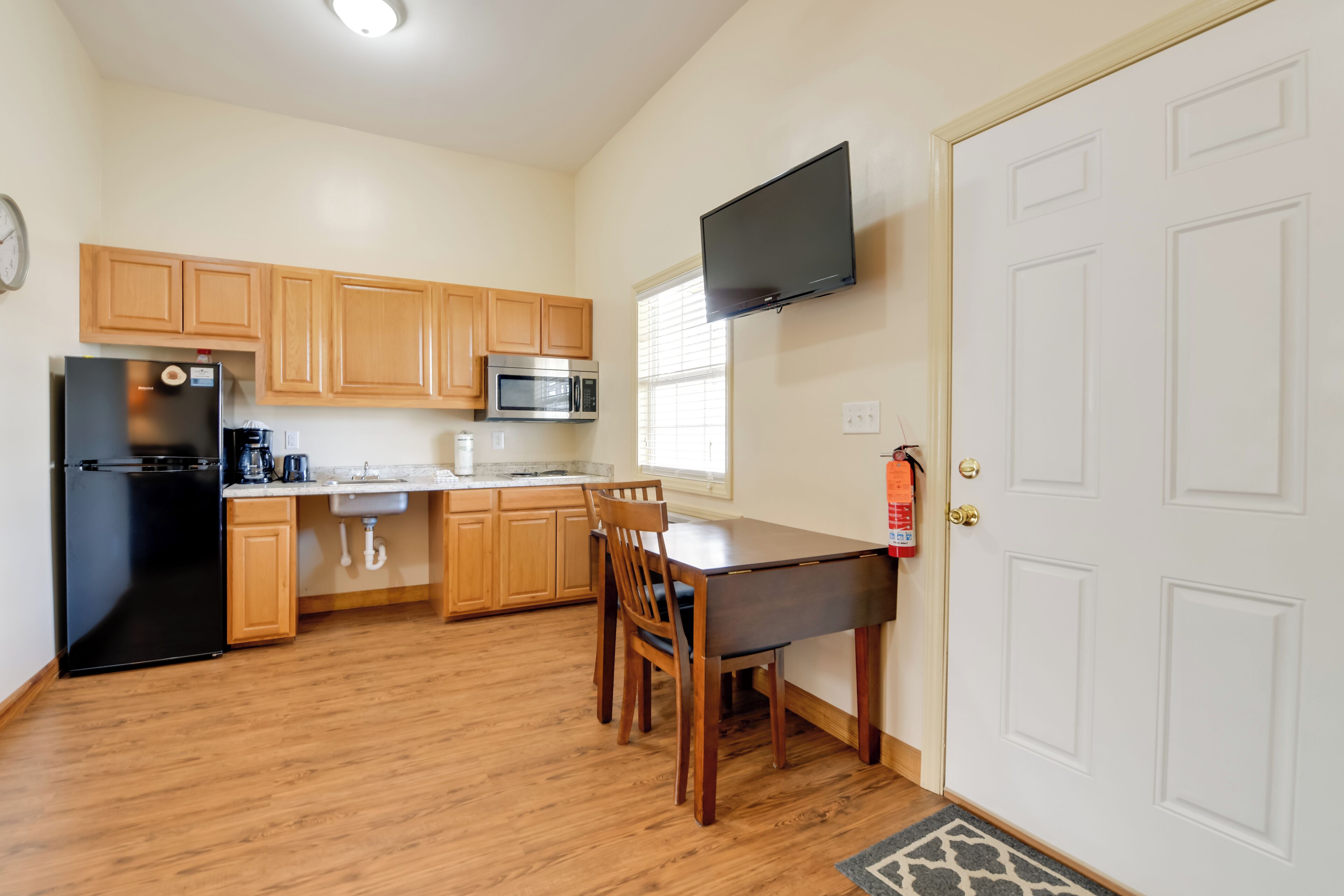 A kitchen with wooden cabinets, a black refrigerator, a microwave, a sink, and a dining table with chairs.
