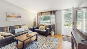A modern living room with a leather sofa, a wooden coffee table, and a TV stand. - 4 BR Home w/ Backyard & Steps From the Lake (Shelton)