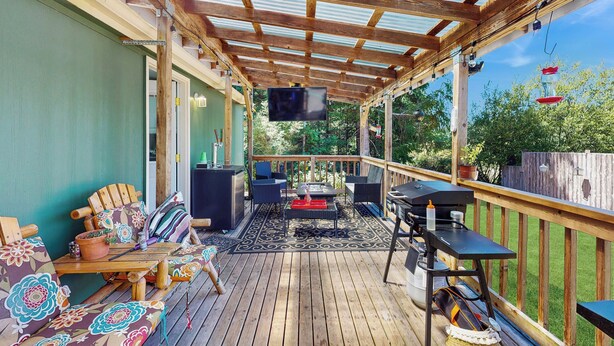A covered deck with wooden furniture, a grill, and a TV. - 4 BR Home w/ Backyard & Steps From the Lake (Shelton)