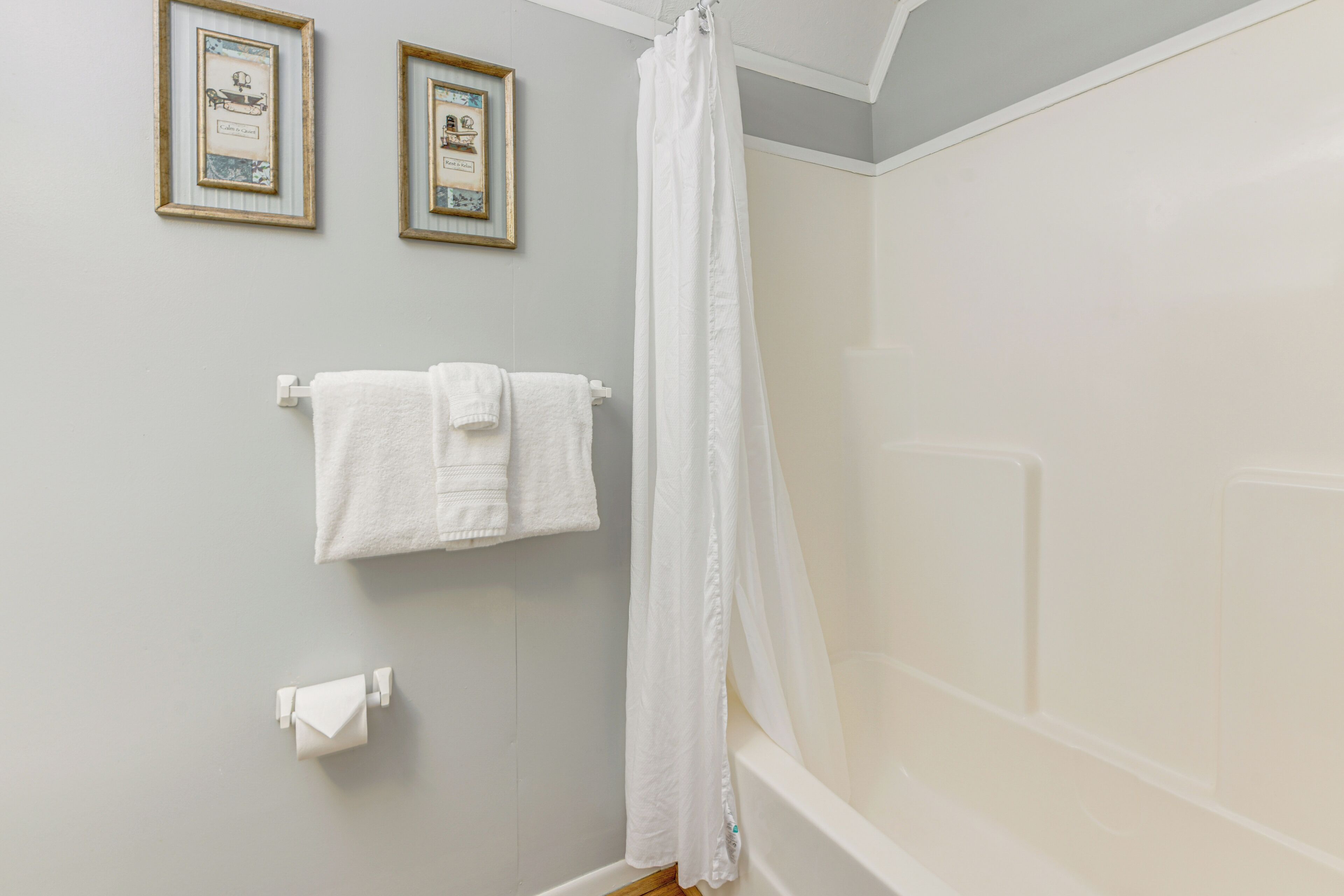 Ein Badezimmer mit einer Badewanne, zwei gerahmten Bildern an der Wand und einem weißen Duschvorhang.