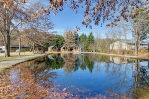 A tranquil pond with reflections, surrounded by trees and a small building with a green roof. - Cataloochee Adventure Hub w/ Family-friendly Perks (Waynesville)