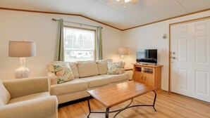 A living room with a sofa, a coffee table, a TV on a wooden stand, a lamp, and a door. - Mtn-view Adventure Hub! Waynesville Home w/ Perks (Waynesville)