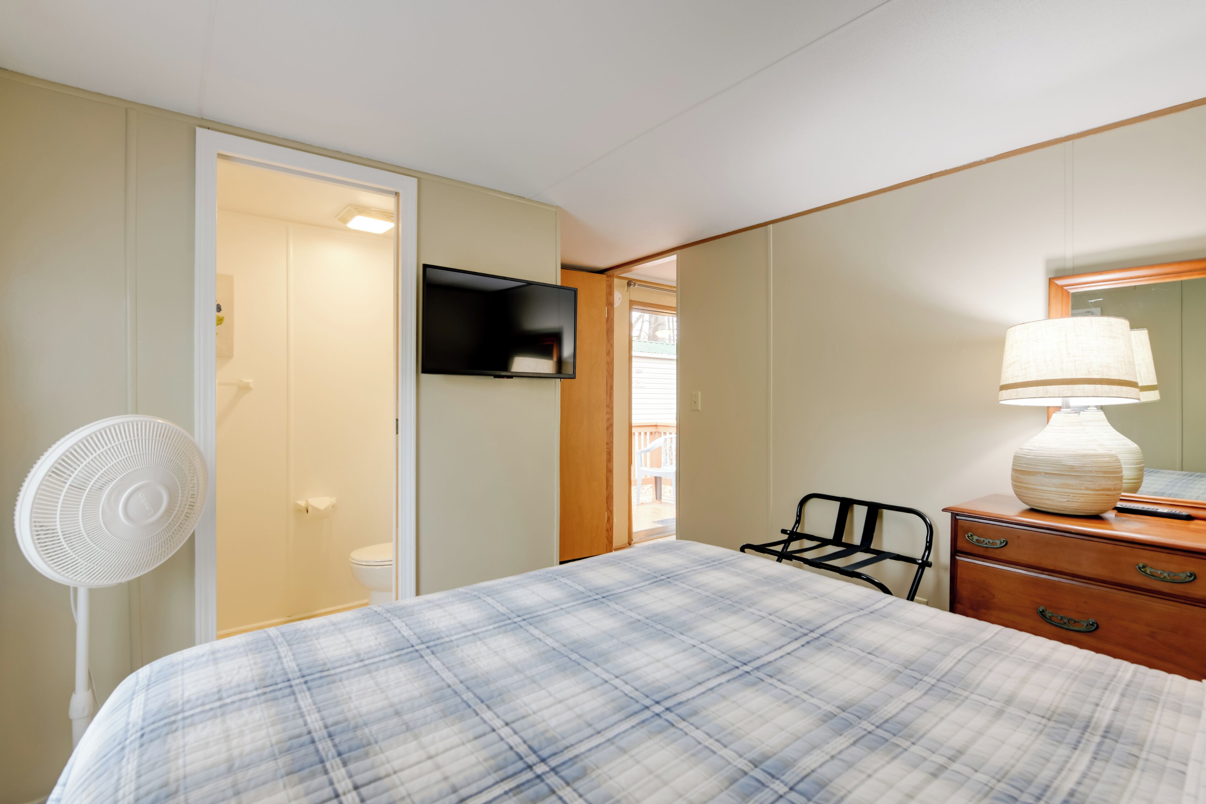 A bedroom with a bed, a dresser, a lamp, a TV, and a fan.