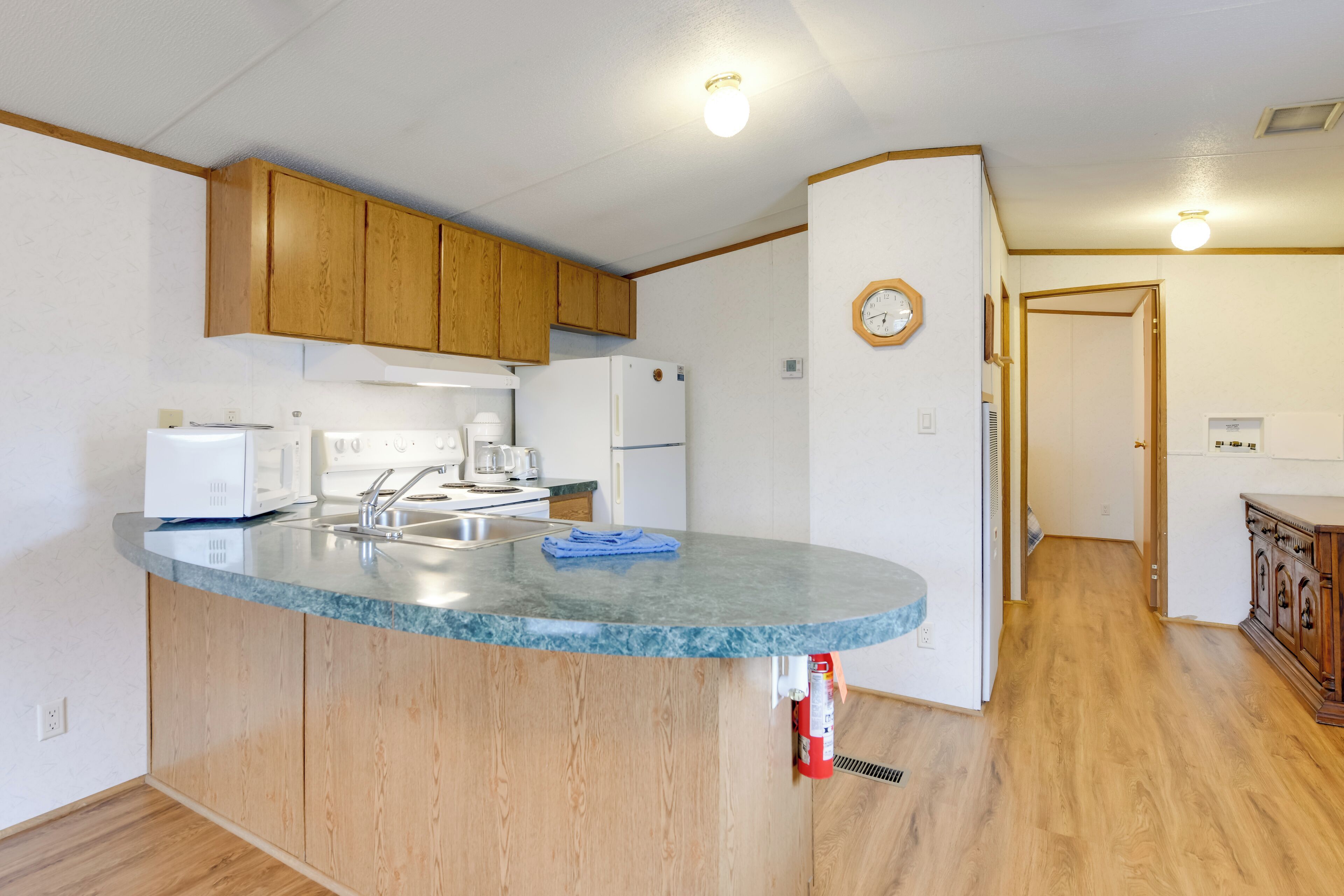 A kitchen with wooden cabinets, a granite countertop, a microwave, a coffee maker, and a clock on the wall.