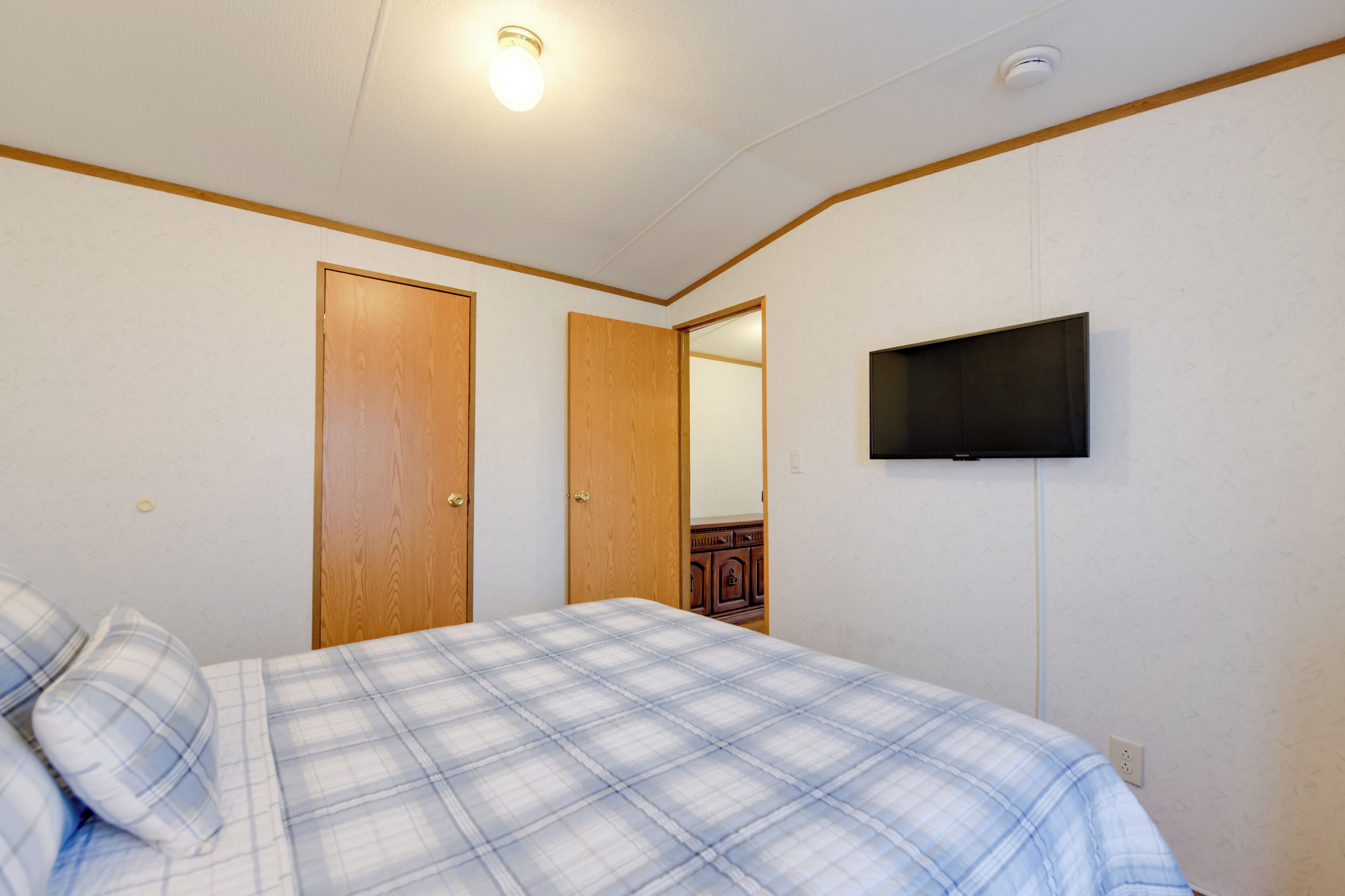 A bedroom with a bed, two wooden doors, a television mounted on the wall, and a ceiling light.