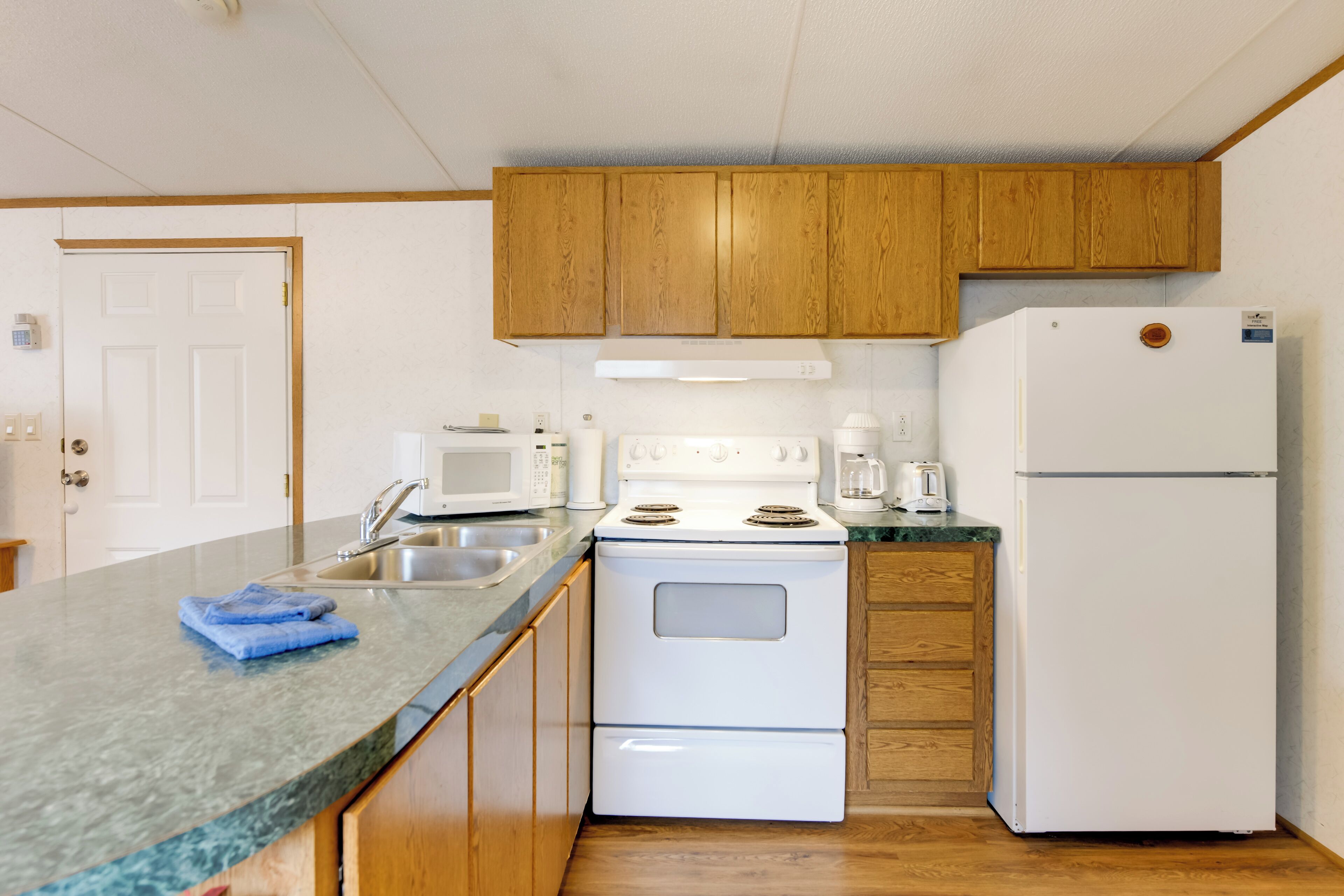 A kitchen with wooden cabinets, a white stove, a microwave, a sink, and a refrigerator.