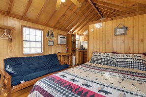 A cozy cabin interior with a bed, a sofa, wooden walls, and a kitchenette. - Blue Ridge Getaway! Studio w/ Resort Amenities (Waynesville)
