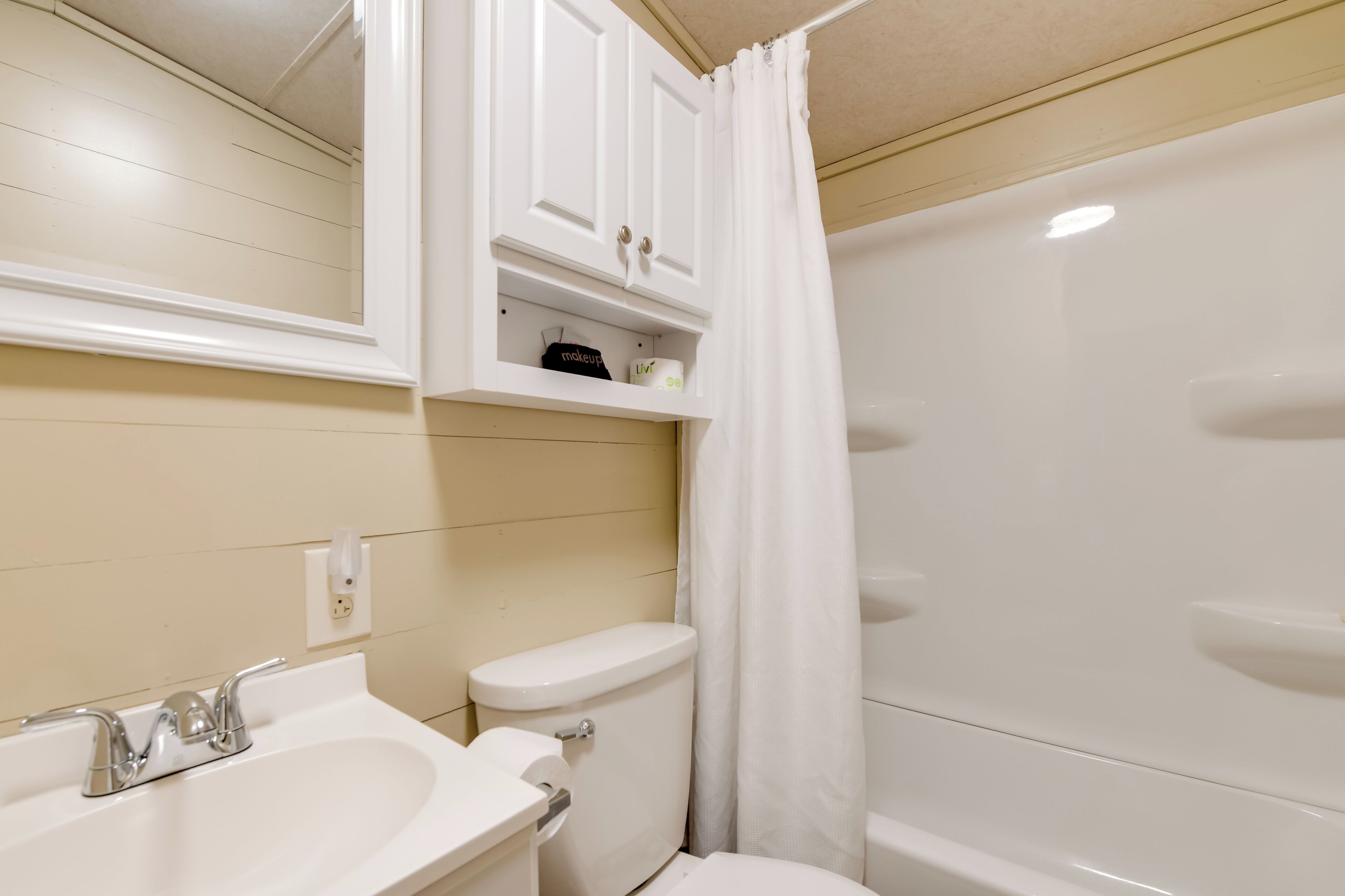 A bathroom with a sink, toilet, and bathtub. There are cabinets above the toilet and a shower curtain.