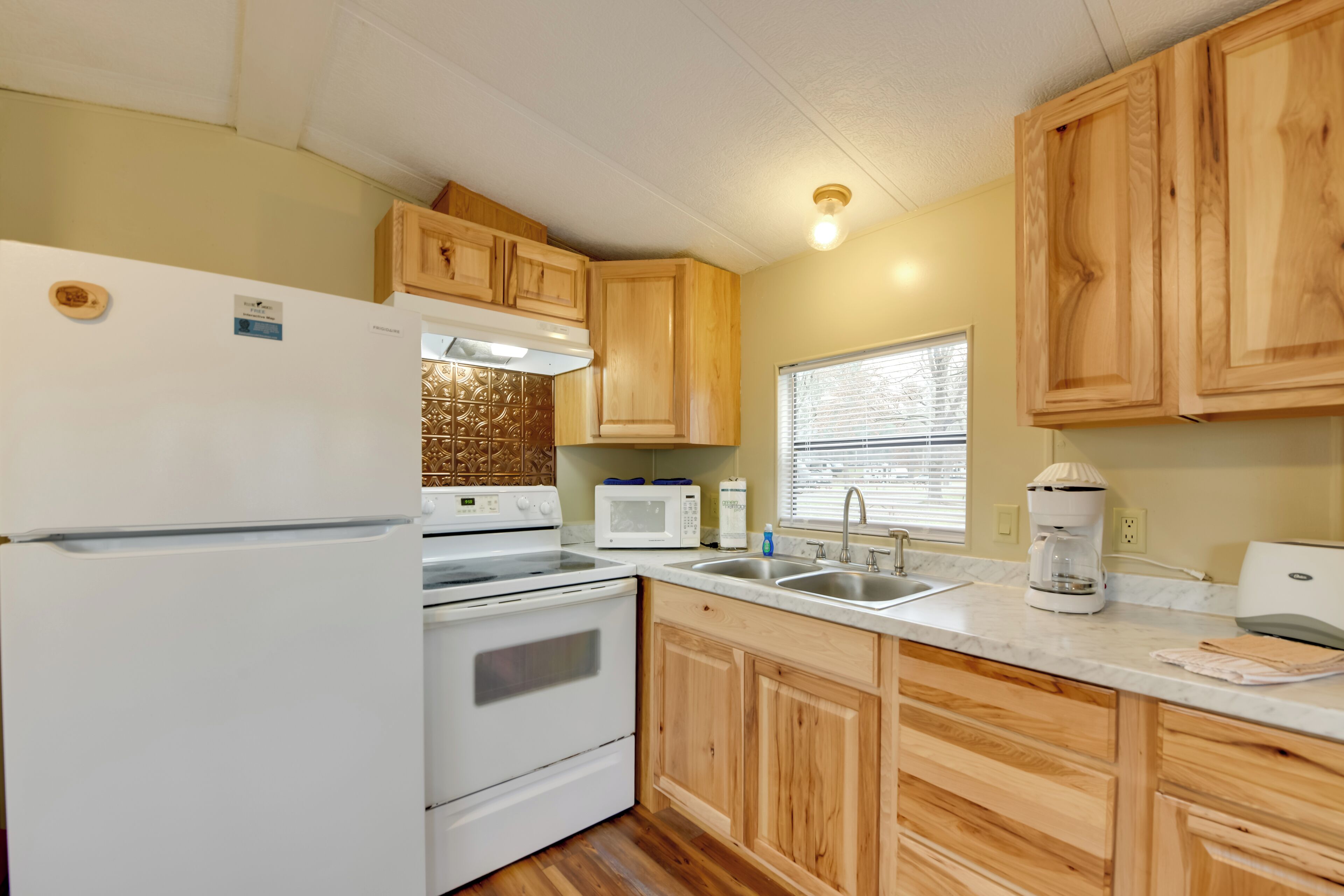 A compact kitchen with wooden cabinets, a white refrigerator, a stove, a microwave, and a coffee maker.