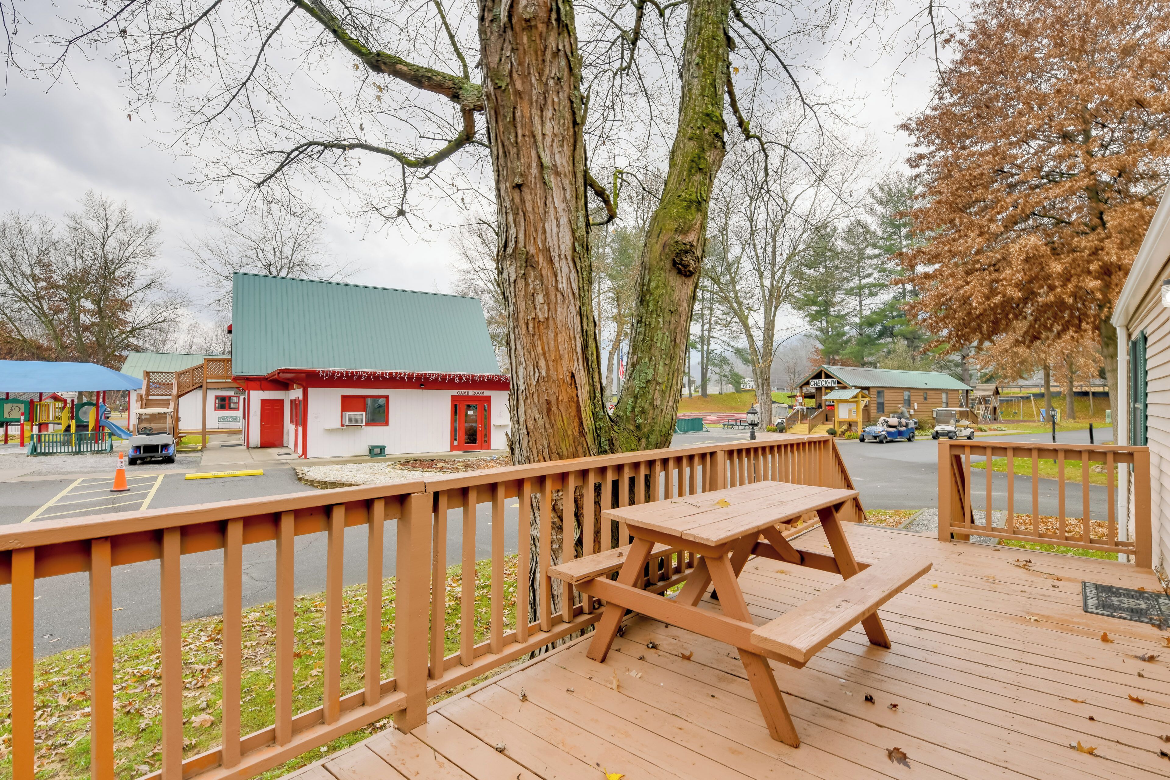 A wooden deck with picnic tables, a playground, and a small building with a red door.