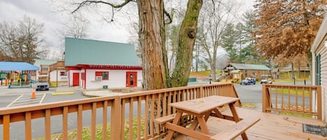 A wooden deck with picnic tables, a playground, and a small building with a red door.