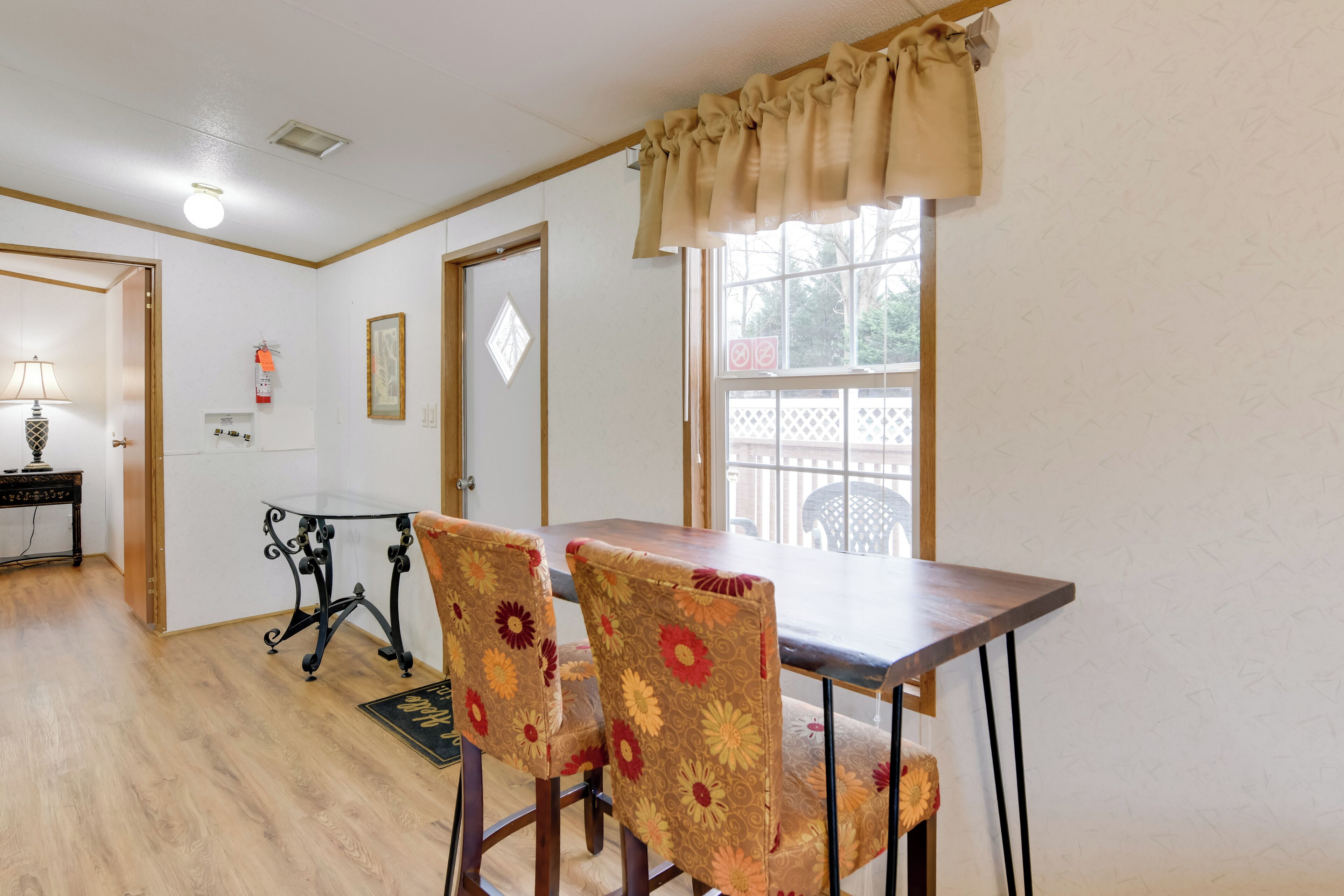 A dining area with a wooden table and floral-patterned chairs, a small side table, and a window with a view of the outside.