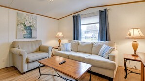 Een woonkamer met een beige bank, een houten salontafel en een schilderij van bloemen aan de muur.