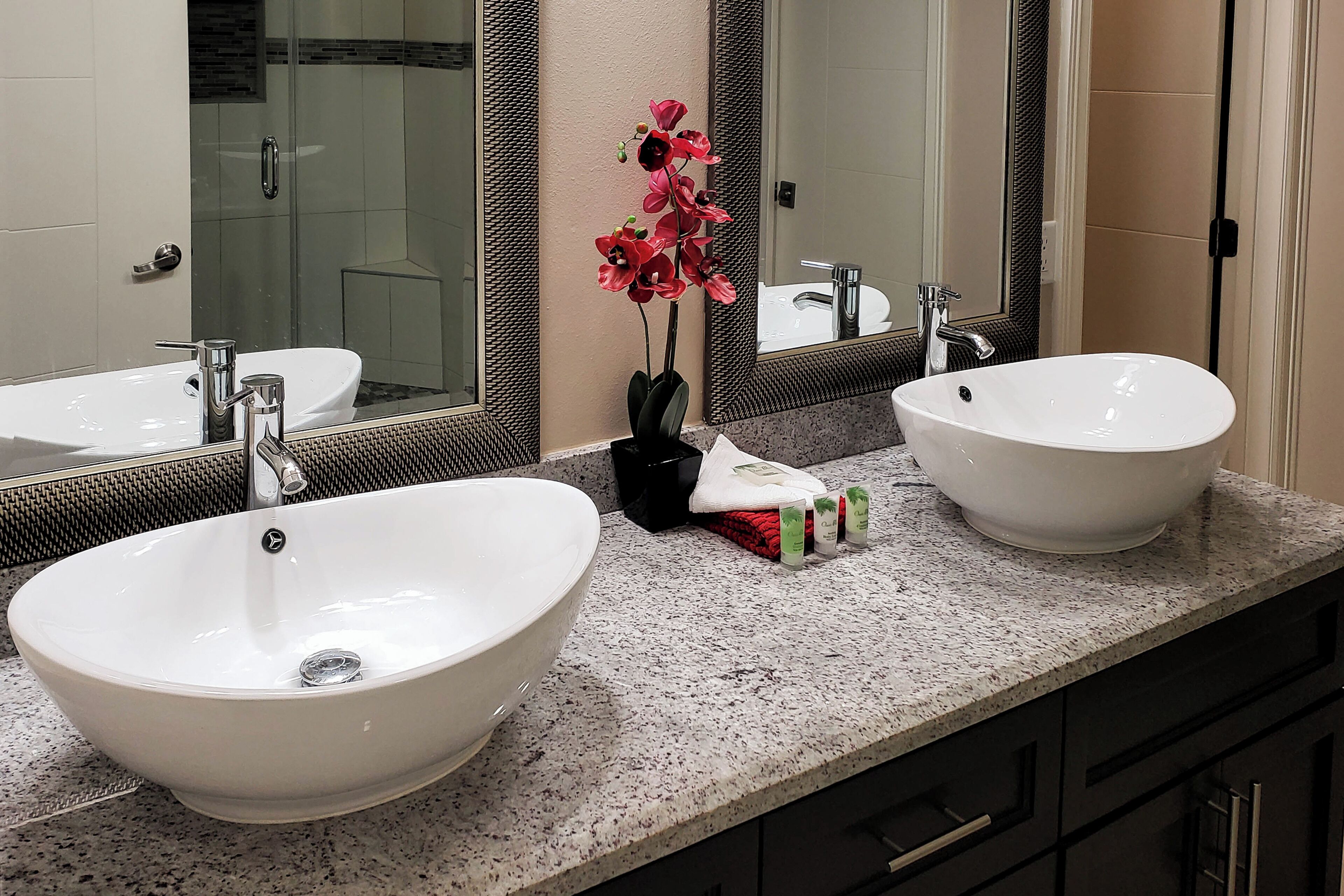 A bathroom with two white sinks, a glass shower enclosure, and a mirror with a textured frame.