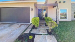 A modern two-story house with a garage, a well-maintained lawn, and a pathway leading to the front door. - Pool, Patio & Yard: Chic South Texas Home (Olmito)
