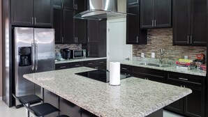 A modern kitchen with dark cabinets, stainless steel appliances, a granite countertop, and bar stools. - Pool, Patio & Yard: Chic South Texas Home (Olmito)