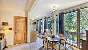 A dining area with a wooden table and chairs, a rug, and a view of the outdoors through large windows. - Sunny Downtown Studio w/ Kitchenette & AC (Fairbanks)