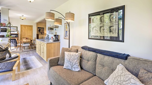 A living room with a sofa, a coffee table, and a dining area with a table and chairs. There is a kitchen area with cabinets and a refrigerator. - Sunny Downtown Studio w/ Kitchenette & AC (Fairbanks)