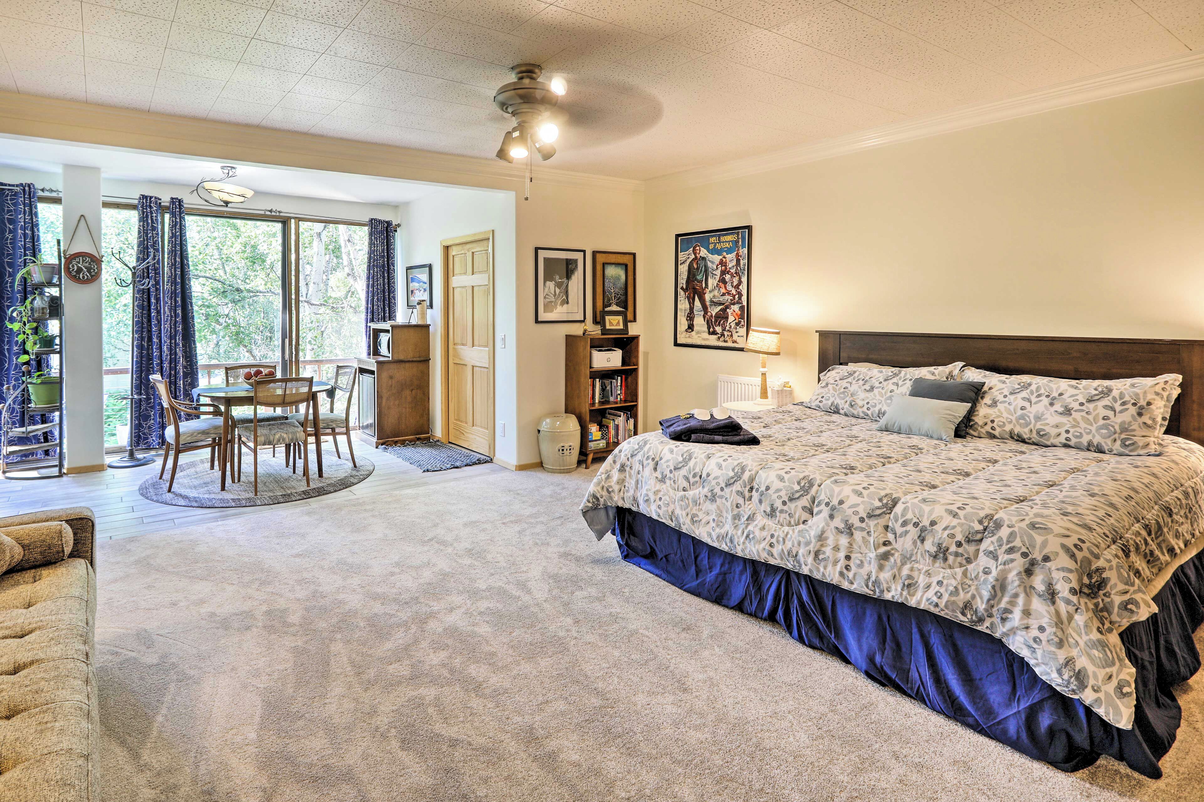 Une chambre avec un grand lit, un bureau avec des chaises, une bibliothèque et une vue à travers une porte vitrée.