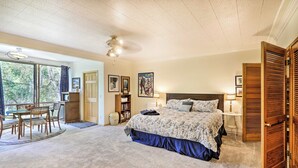 A bedroom with a large bed, a desk, and a bookshelf. There is a window with curtains and a door with a wooden shutter. - Sunny Downtown Studio w/ Kitchenette & AC (Fairbanks)