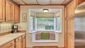 A kitchen with wooden cabinets, a built-in bench with pillows, a window, and a refrigerator. - Vibrant 3BR Near Downtown w/ Fireplaces (Fairbanks)