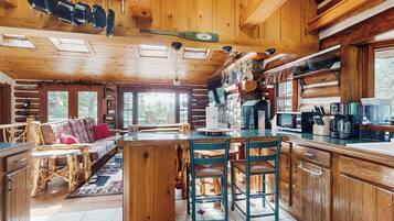 Ein rustikales Blockhaus-Interieur mit einer Essnische aus Holz, einer zentralen Kochinsel und einer Küche mit modernen Geräten.