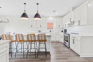 A modern kitchen with white cabinetry, a central island with bar stools, pendant lighting, and a view to the outside.