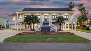 A two-story building with a central staircase, a covered front porch, and a landscaped front yard with palm trees. - Bring Your Boat! Lake Charles Home w/ Dock & Lift (Lake Charles)