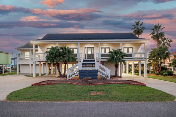 A two-story building with a central staircase, a covered front porch, and a landscaped front yard with palm trees.