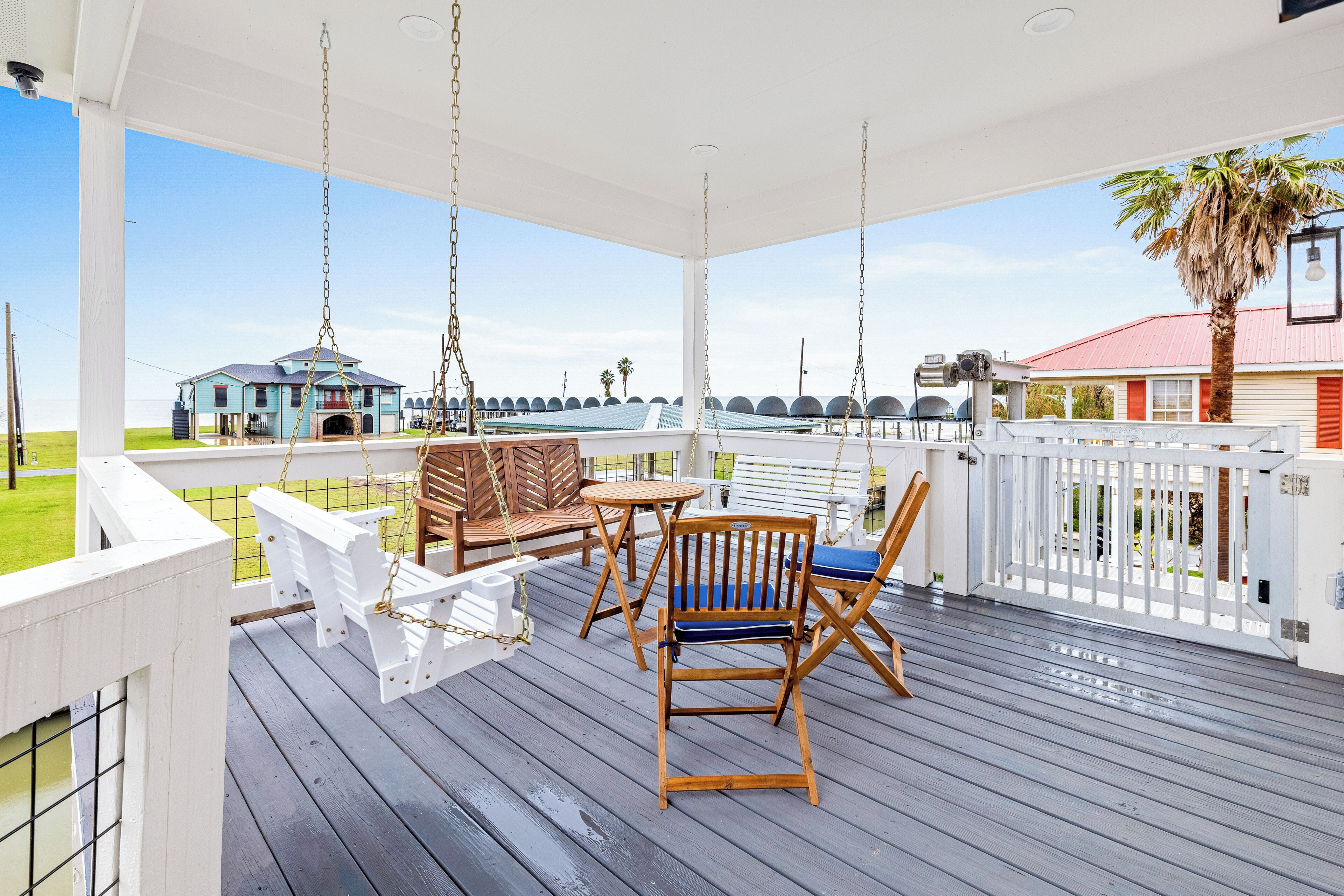 A covered outdoor deck with wooden furniture, a swing, and a view of a building with a red roof.
