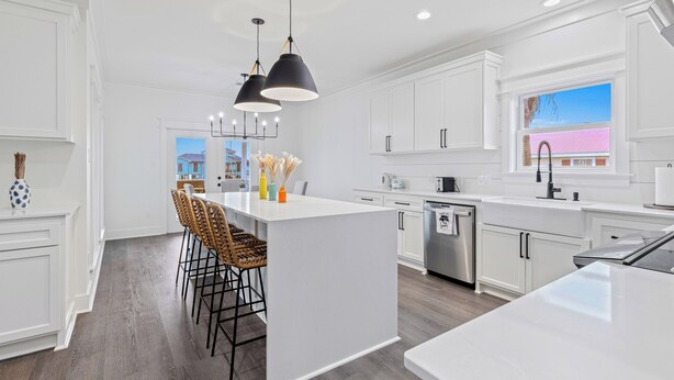 A modern kitchen with white cabinetry, a central island with bar stools, pendant lighting, and a view of a pink building through a window. - Bring Your Boat! Lake Charles Home w/ Dock & Lift (Lake Charles)