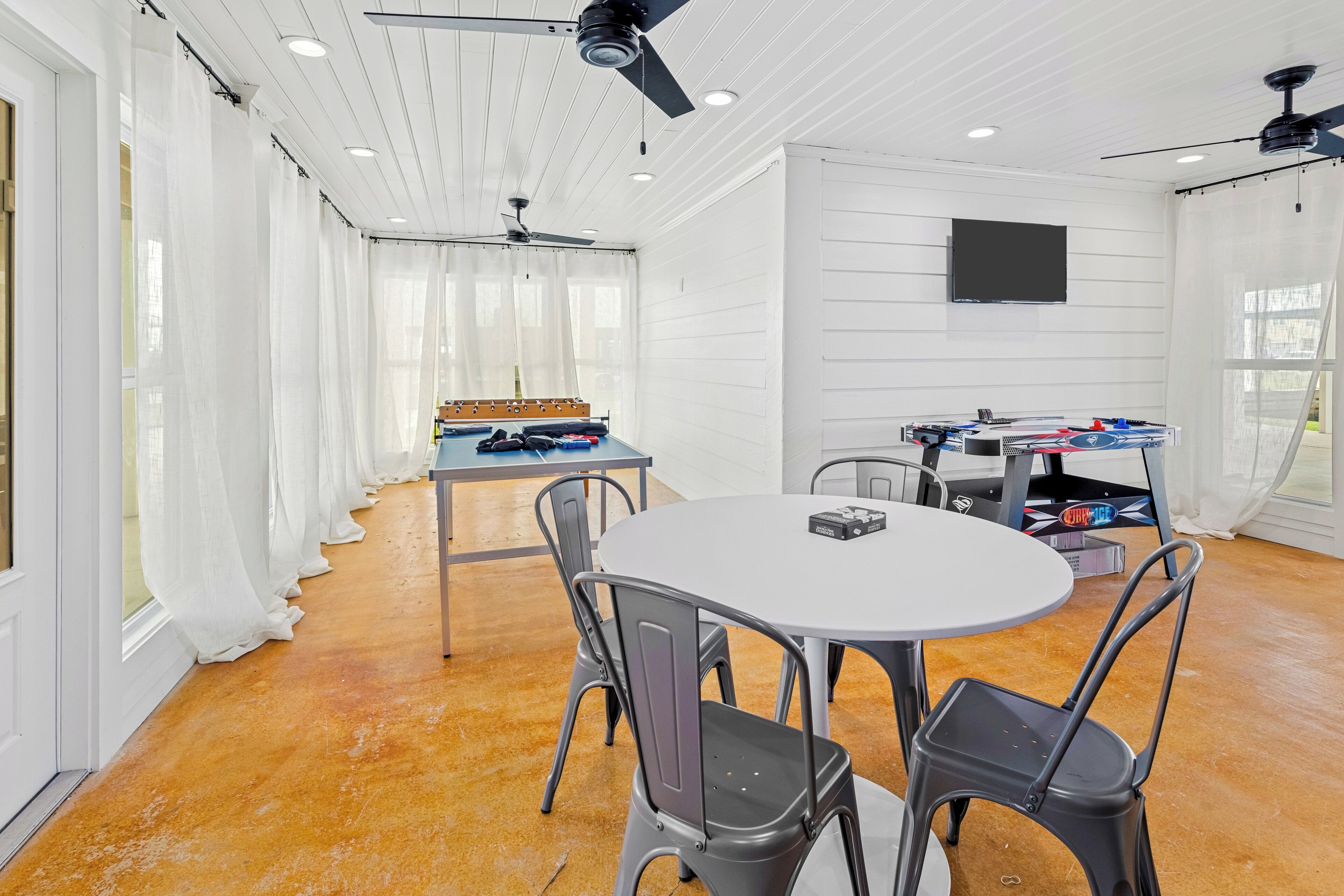 Ein geräumiges Zimmer mit einem runden Tisch, Stühlen, Deckenventilatoren und einem an der Wand befestigten Fernseher.