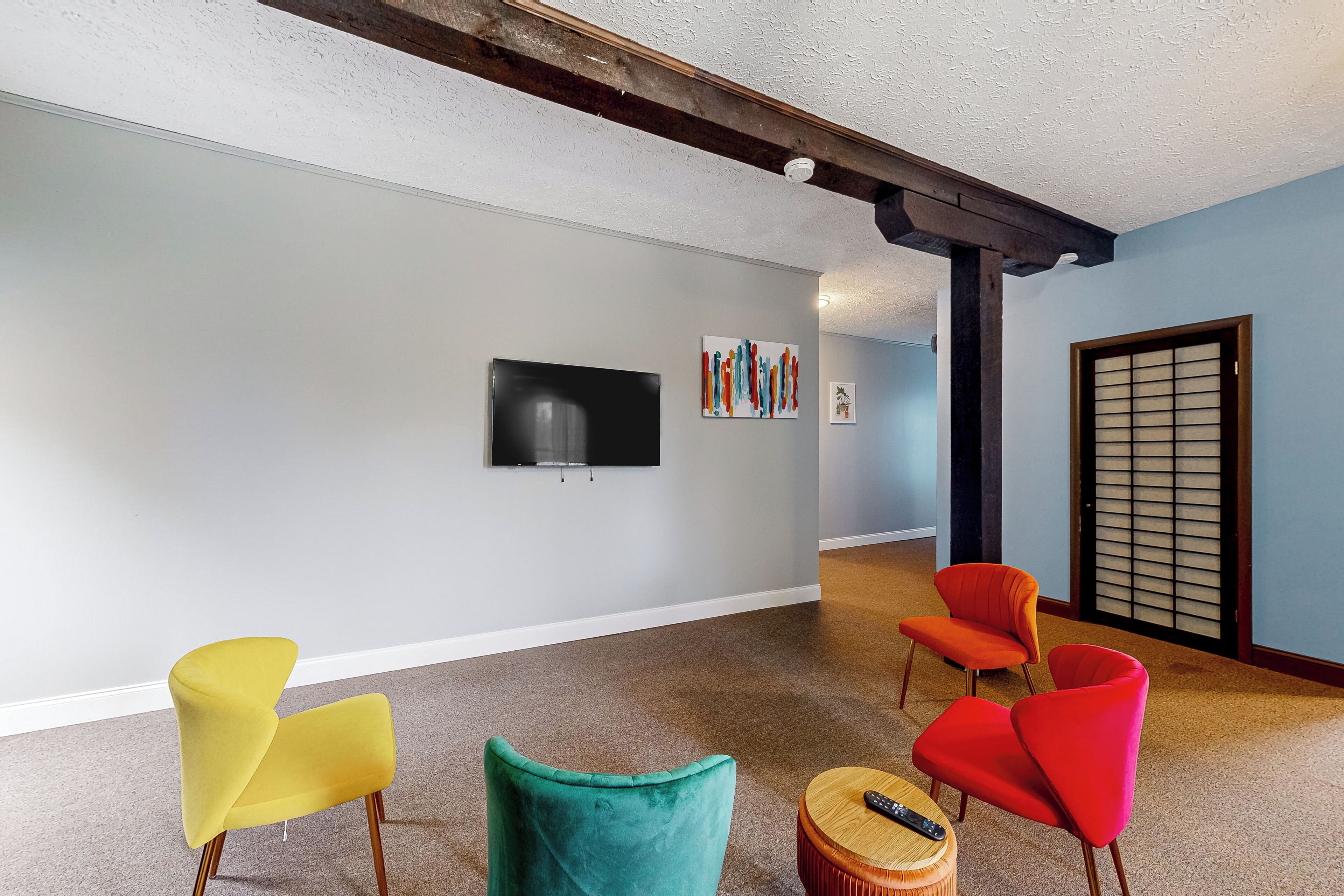 A room with a TV, colorful artwork, and three chairs.