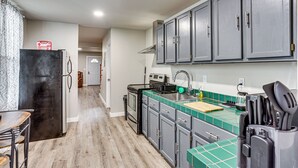 Una cocina con armarios grises, un refrigerador negro, una estufa y una encimera con azulejos verdes.