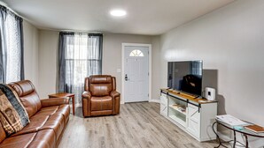 Una sala de estar con un sofá de cuero marrón, un sillón de cuero, una mesa de centro de madera, un televisor sobre un mueble bajo y un armario blanco con puertas de vidrio.