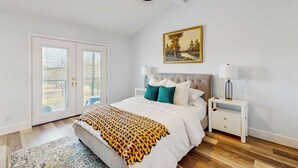 A bedroom with a bed, nightstands, a ceiling fan, a painting, and a view through the glass doors. - Modern Living in Texas! Home 2 Blocks to Lake LBJ (Marble Falls)