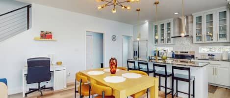 A modern kitchen with white cabinets, a central island, and a dining area with a yellow table and chairs.