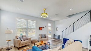 A spacious living room with a high ceiling, a staircase, and a large window with blinds. - Modern Living in Texas! Home 2 Blocks to Lake LBJ (Marble Falls)