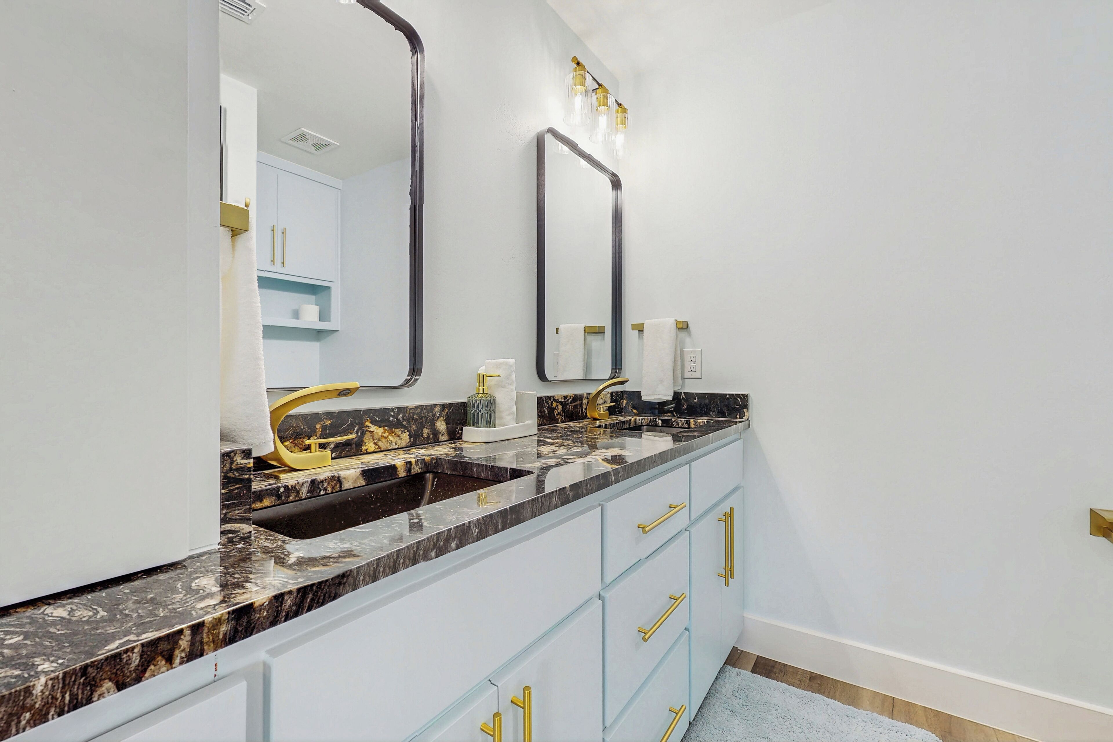 Un baño con lavamanos de mármol, detalles dorados y armarios azul claro.